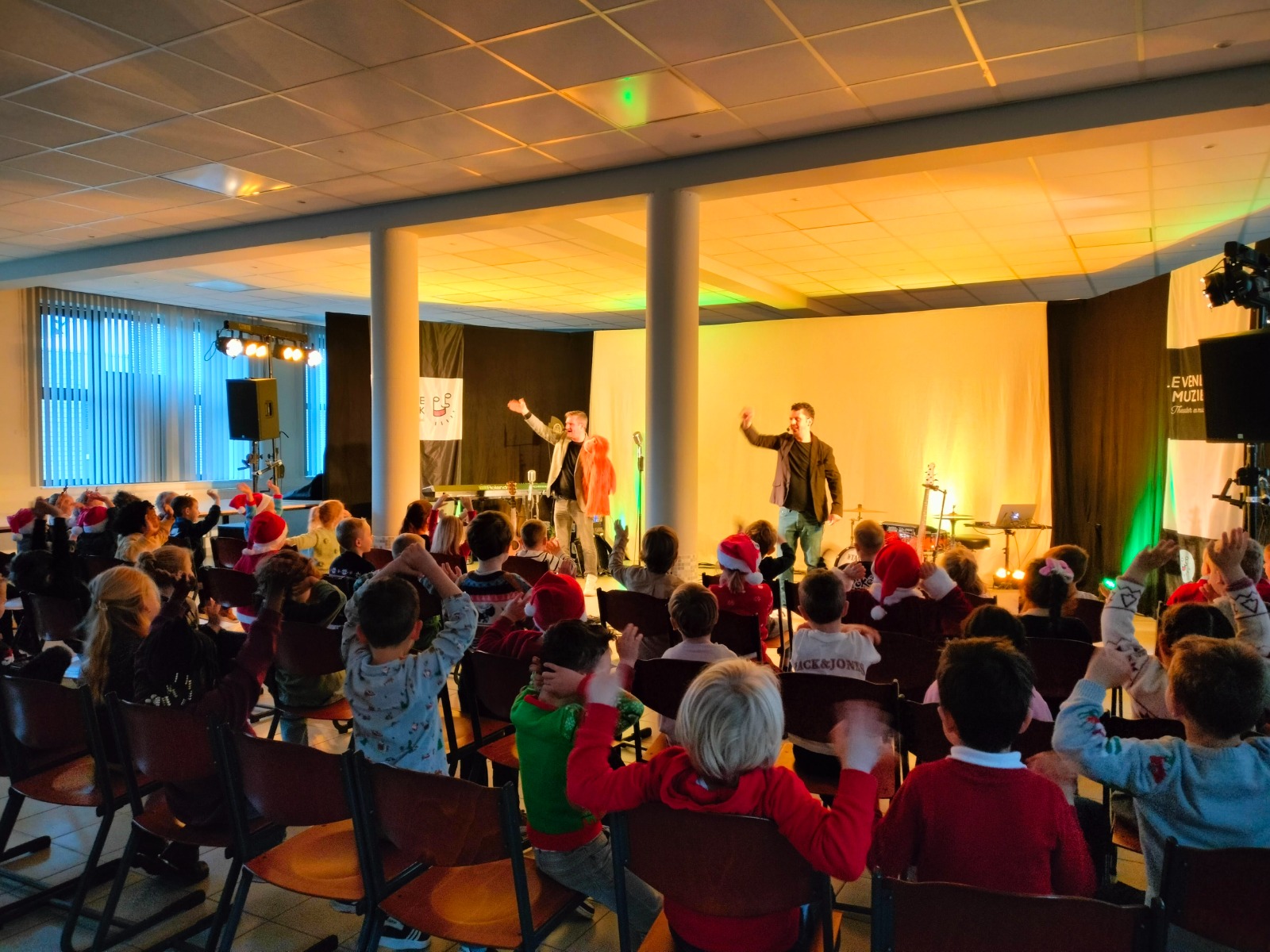 Twee muzikanten zwaaien voor een publiek van kleuters. 